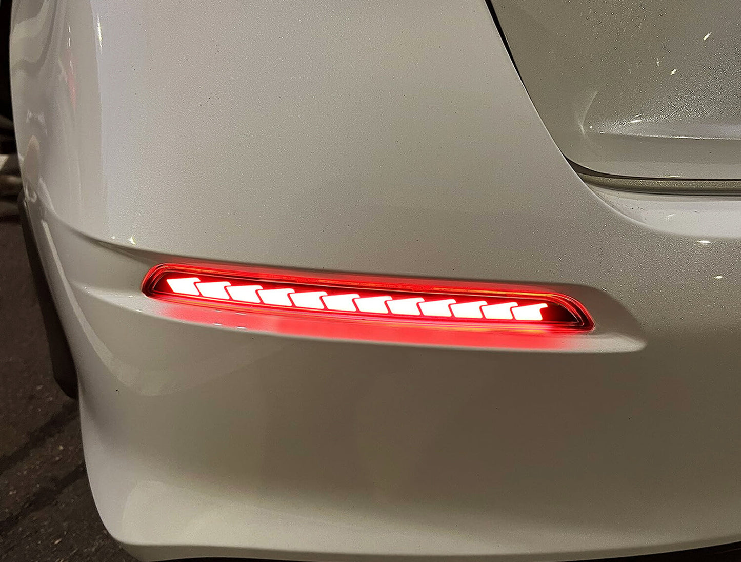 Close-up rear bumper detail of glowing red sequential reflector on white 2022+ Honda Civic Sedan
